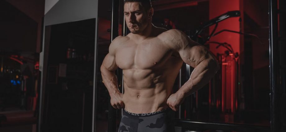 Shirtless bodybuilder flexing muscles under dramatic gym lighting. Fitness and strength.